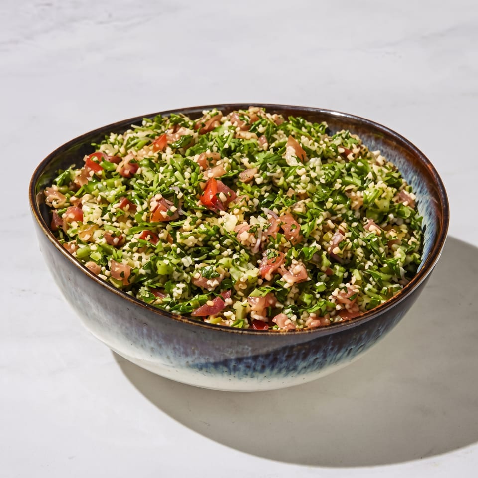 Bowl of tabbouleh salad with bulgur, chopped parsley, tomatoes, and green vegetables on a ceramic plate.