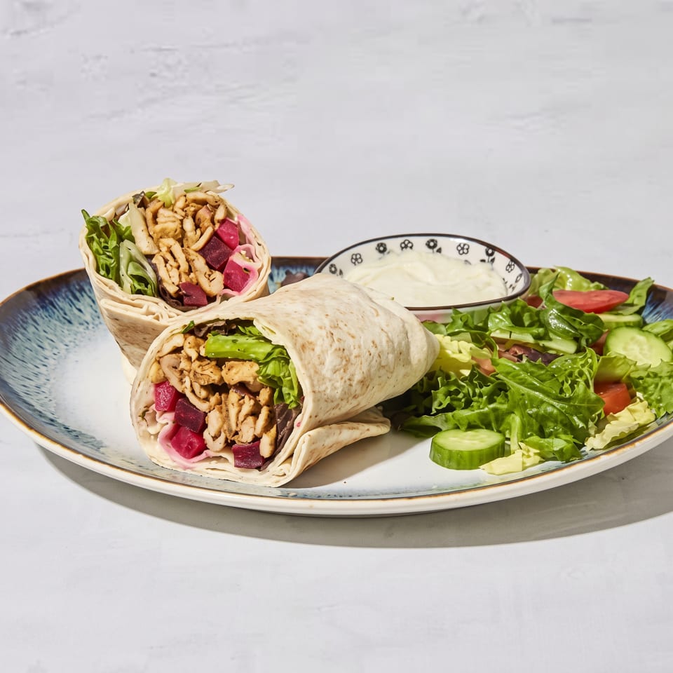 Two stuffed flatbread wraps with crispy filling, greens, pickled vegetables, salad, and creamy dip on a decorative plate.