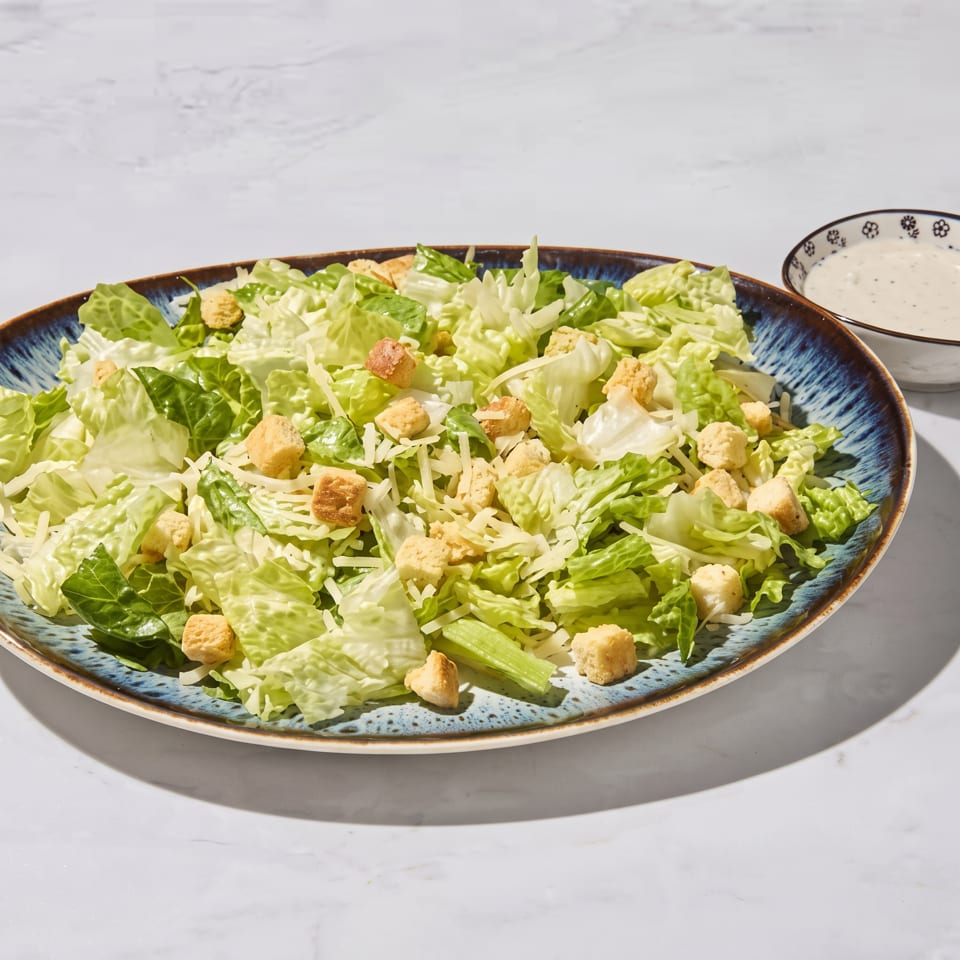 Crisp green salad with croutons and shredded cheese on a blue plate, accompanied by a bowl of creamy dressing.